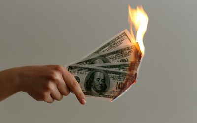 Hand holding burning money, symbolizing government waste and lost taxpayer dollars.