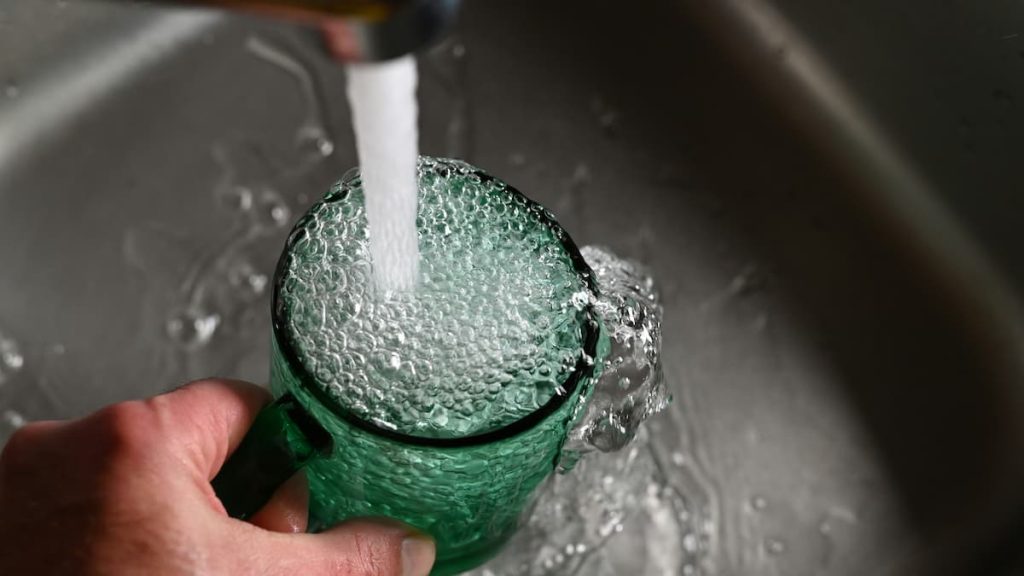 Clear glass being filled with tap water from a kitchen faucet.