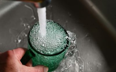 Clear glass being filled with tap water from a kitchen faucet.