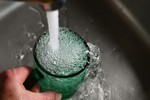 Clear glass being filled with tap water from a kitchen faucet.
