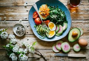 Image of a bowl containing fruits, salad and eggs sitting on a wooden table.