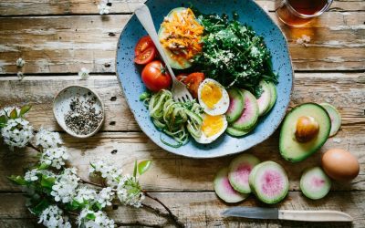 Image of a bowl containing fruits, salad and eggs sitting on a wooden table.