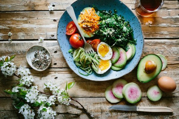 Image of a bowl containing fruits, salad and eggs sitting on a wooden table.
