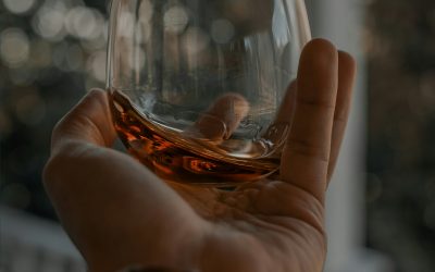 A man’s hand holding a glass of whiskey on an outdoor balcony.