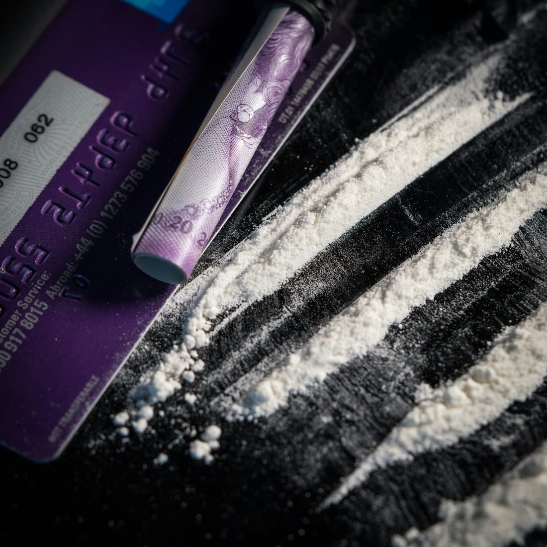 Close-up of illicit substances arranged on a flat surface, alongside a credit card and a makeshift straw.