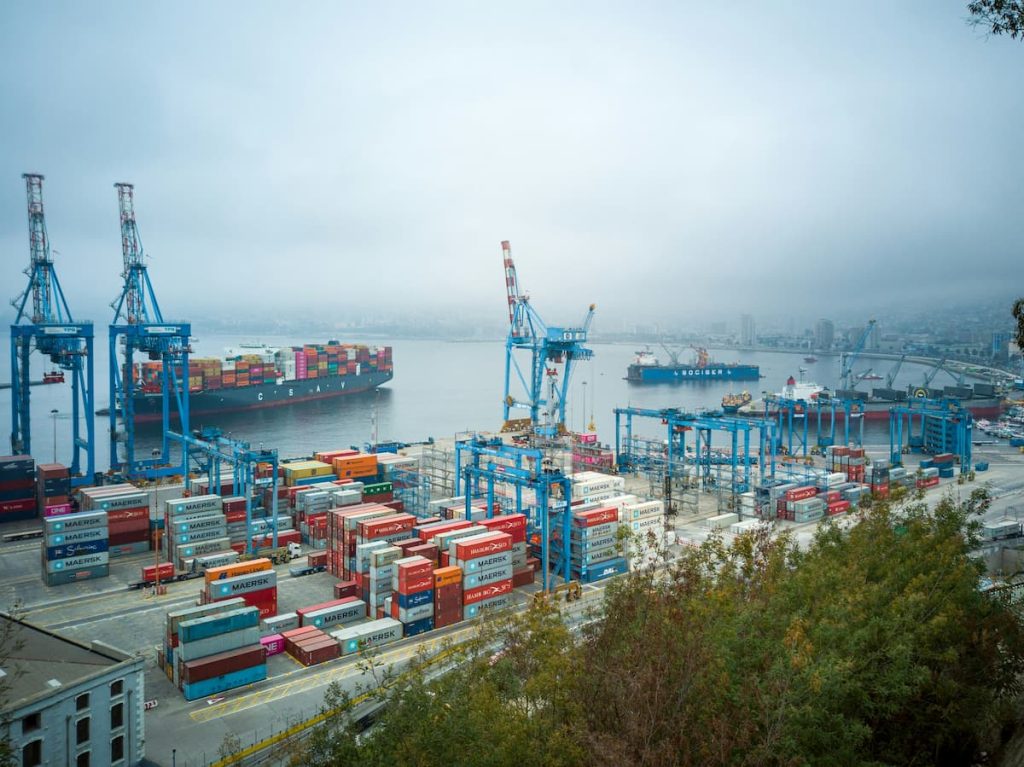 Shipping port with stacked cargo containers and large cranes loading and unloading goods along the dock.