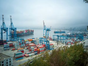 Shipping port with stacked cargo containers and large cranes loading and unloading goods along the dock.