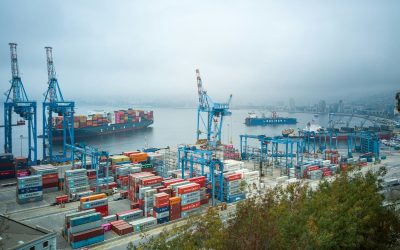 Shipping port with stacked cargo containers and large cranes loading and unloading goods along the dock.