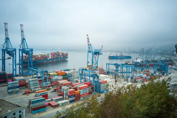 Shipping port with stacked cargo containers and large cranes loading and unloading goods along the dock.