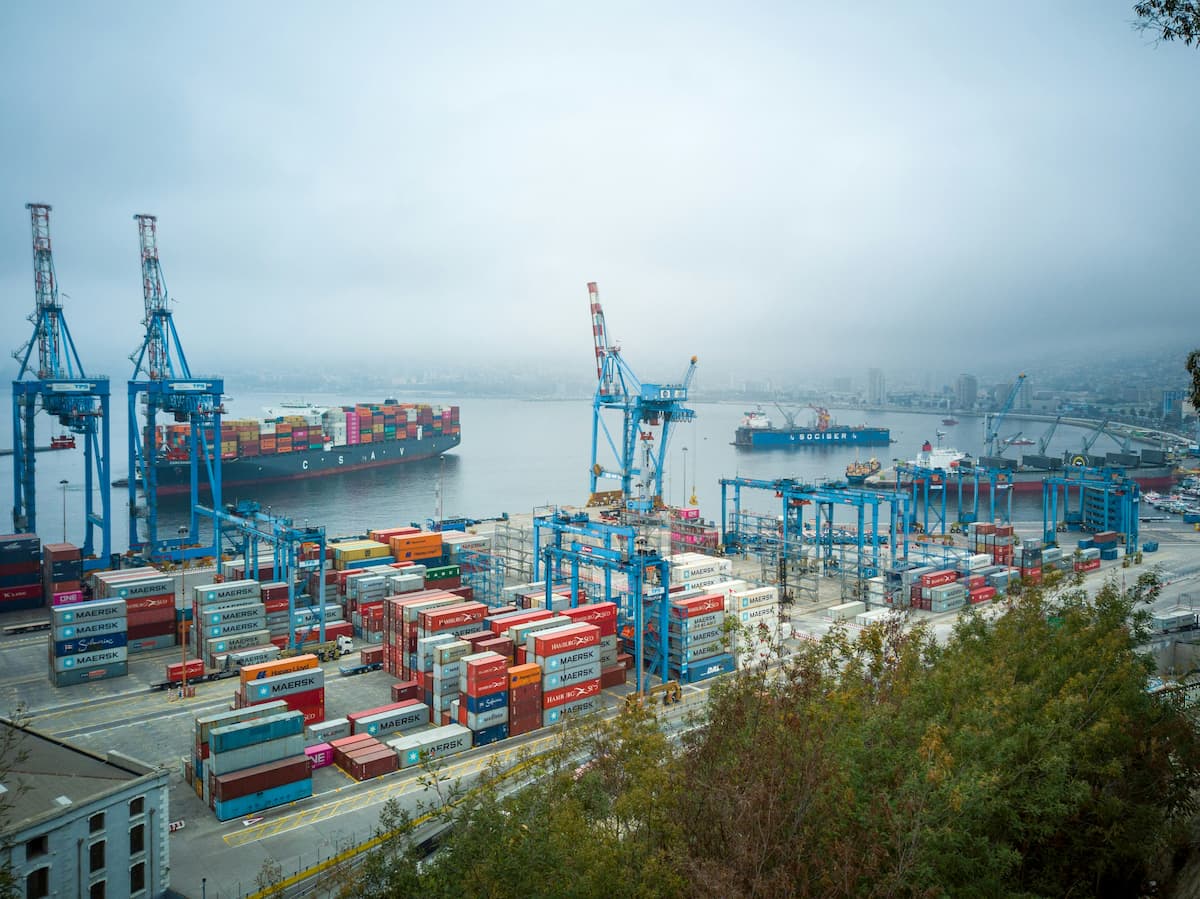 Shipping port with stacked cargo containers and large cranes loading and unloading goods along the dock.