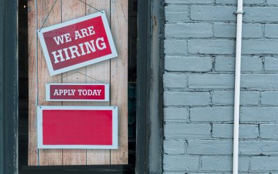 Image of a sign saying 'we are hiring', 'Apply now' in the door window of a store.