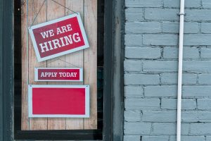 Image of a sign saying 'we are hiring' in the window of a store.