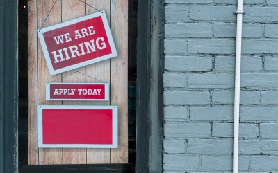 Image of a sign saying 'we are hiring' in the window of a store.