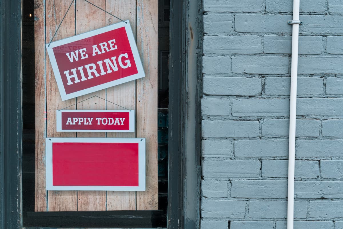 Image of a sign saying 'we are hiring' in the window of a store.