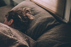 Woman sleeping in bed under blankets, viewed from behind.