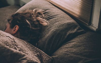 Woman sleeping in bed under blankets, viewed from behind.