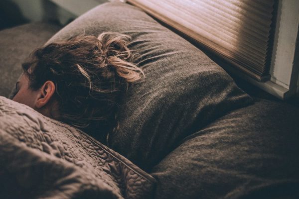 Woman sleeping in bed under blankets, viewed from behind.