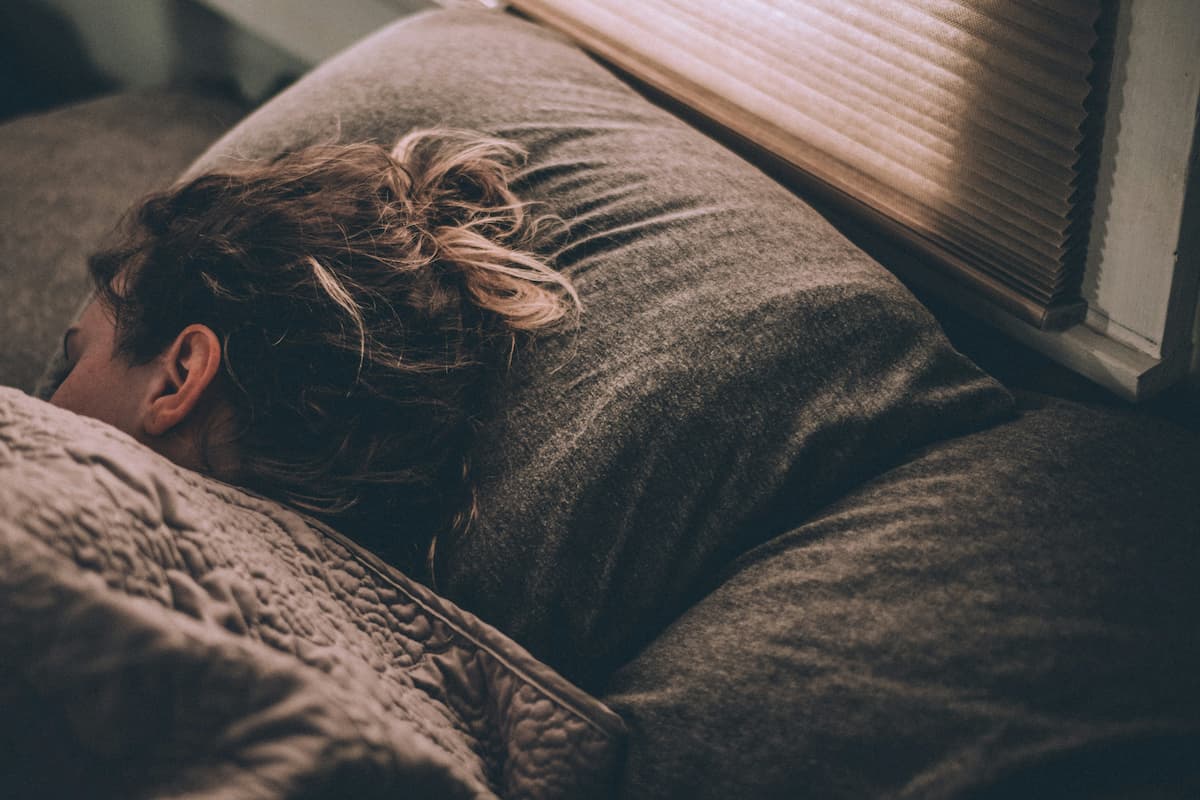 Woman sleeping in bed under blankets, viewed from behind.