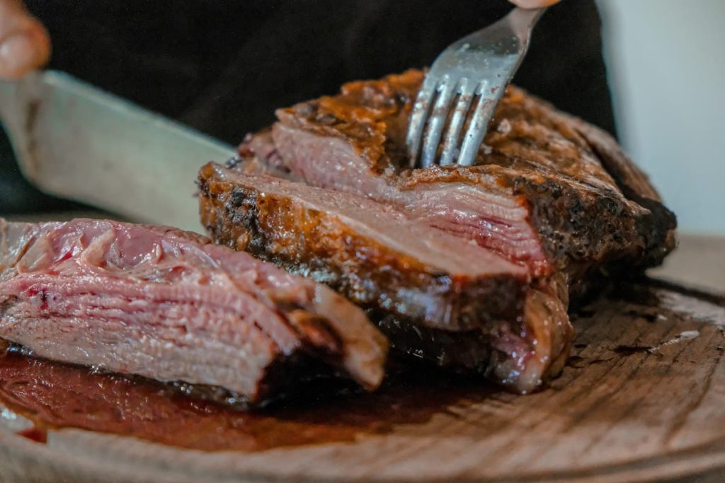 Close up of a cooked steak being cut with a knife and fork.