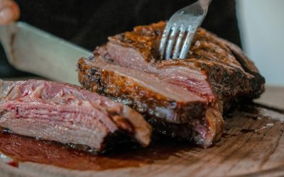 Close up of a cooked steak being cut with a knife and fork.