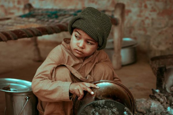 Image of a child living in poverty, cleaning dishes in the streets.
