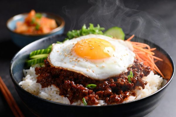 Juicy ground beef in a glossy, sticky garlic-ginger sauce served over steaming white jasmine rice. Topped with a sunny-side-up fried egg, shredded carrots, cucumber slices, green onions, and sesame seeds.