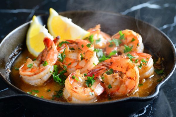 Garlic butter shrimp in a black cast iron skillet – large, plump, golden-seared shrimp sizzling in a rich, glossy garlic butter sauce, garnished with fresh chopped parsley and bright lemon wedges, with gentle steam rising.