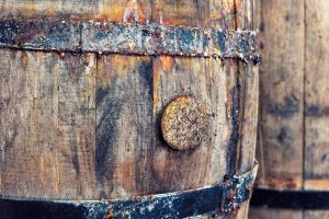 Close-up of a weathered wooden barrel with rusted iron hoops and a cracked bung in the stave.