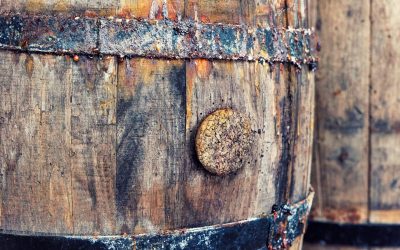Close-up of a weathered wooden barrel with rusted iron hoops and a cracked bung in the stave.