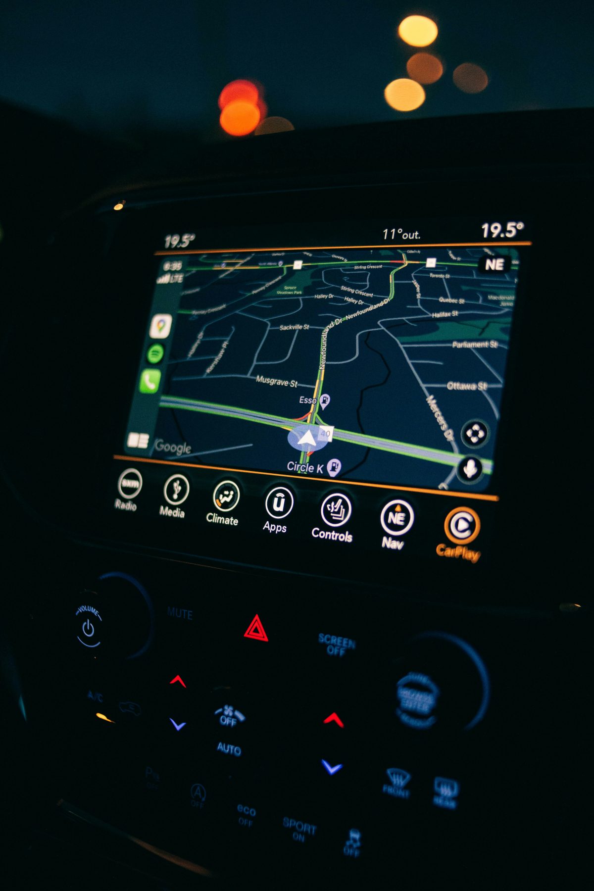Close-up of a car’s infotainment screen showing a GPS navigation map at night, with temperature readings, Google Maps interface, and illuminated climate and media controls on the dashboard.
