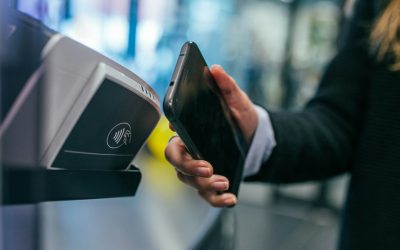 Close-up of a hand holding a smartphone up to a contactless card reader, illustrating cashless digital payment.