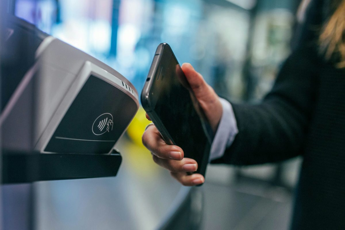 Close-up of a hand holding a smartphone up to a contactless card reader, illustrating cashless digital payment.