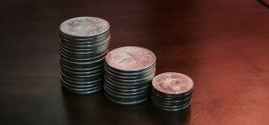 Three stacks of silver coins of increasing height on a dark wooden table, representing the growth of savings through compound interest.