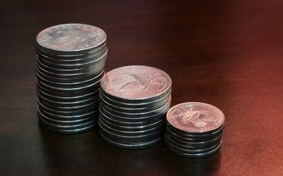 Three stacks of silver coins of increasing height on a dark wooden table, representing the growth of savings through compound interest.