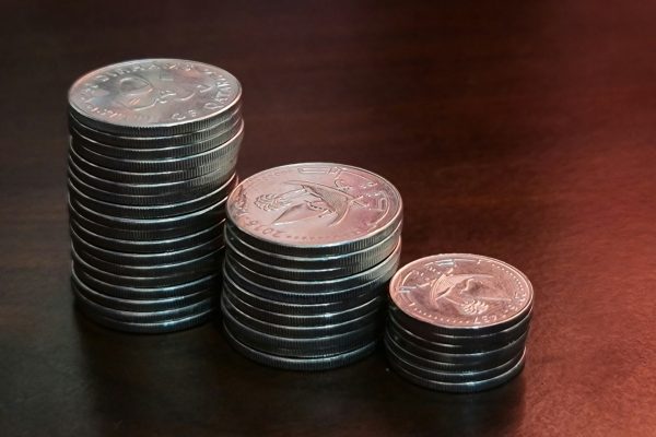Three stacks of silver coins of increasing height on a dark wooden table, representing the growth of savings through compound interest.