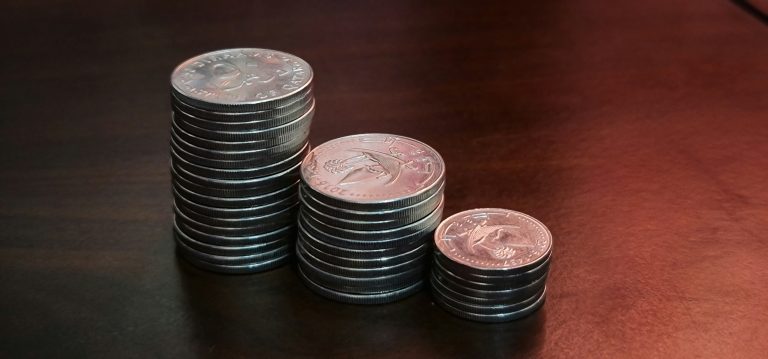 Three stacks of silver coins of increasing height on a dark wooden table, representing the growth of savings through compound interest.