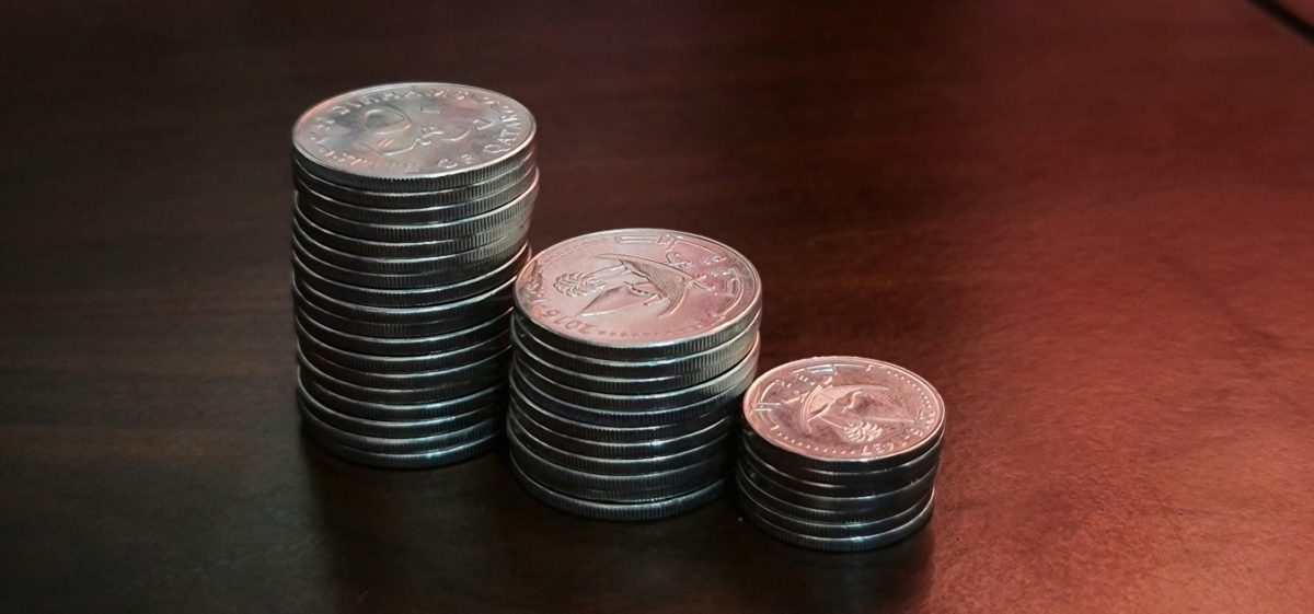 Three stacks of silver coins of increasing height on a dark wooden table, representing the growth of savings through compound interest.