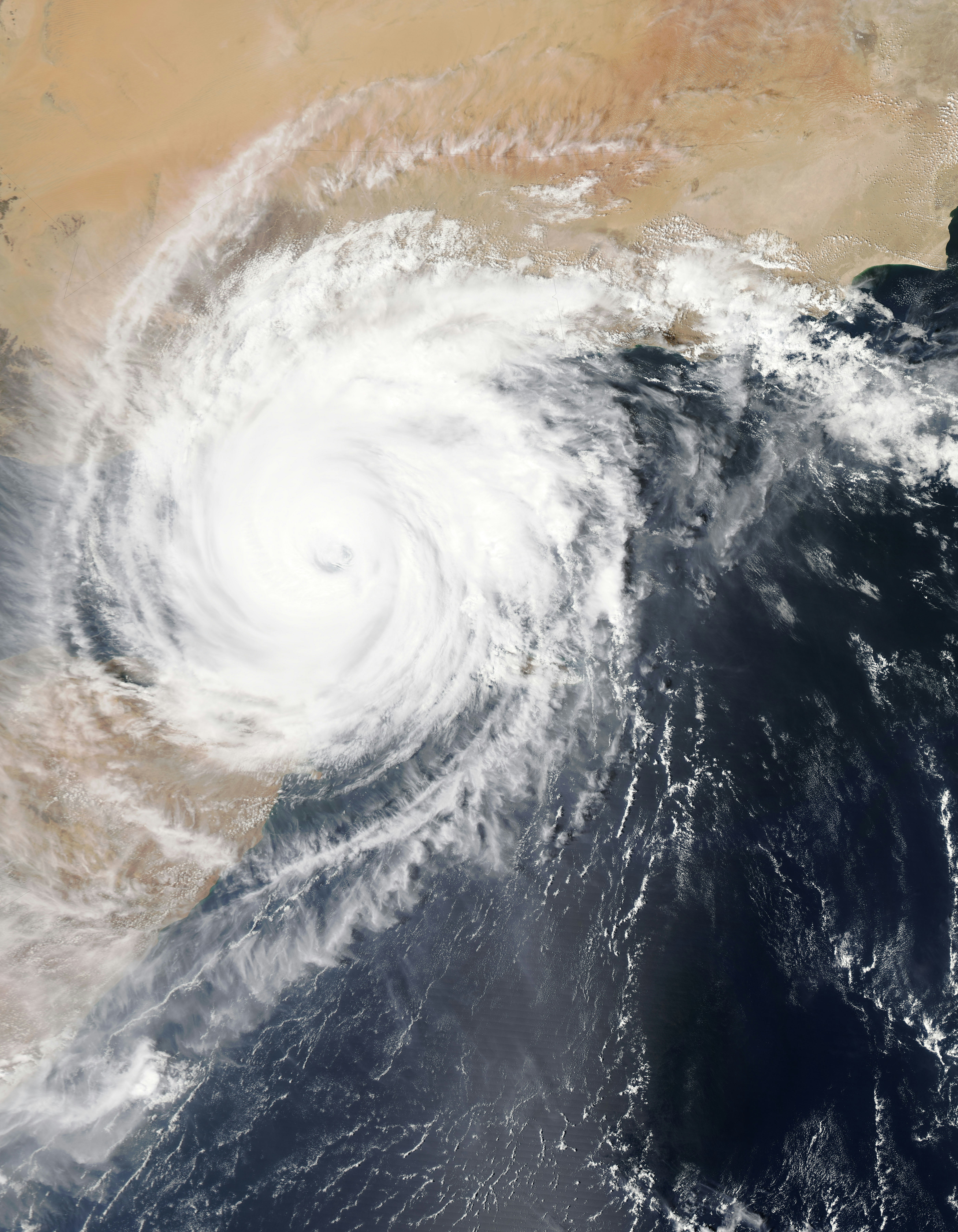 Satellite image of a large, well-formed typhoon with a distinct circular eye and tightly wound white spiral cloud bands over dark blue ocean waters, approaching the coastline.
