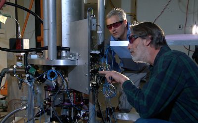 Two scientists standing beside the tall NIST-F2 cesium fountain atomic clock in a laboratory.