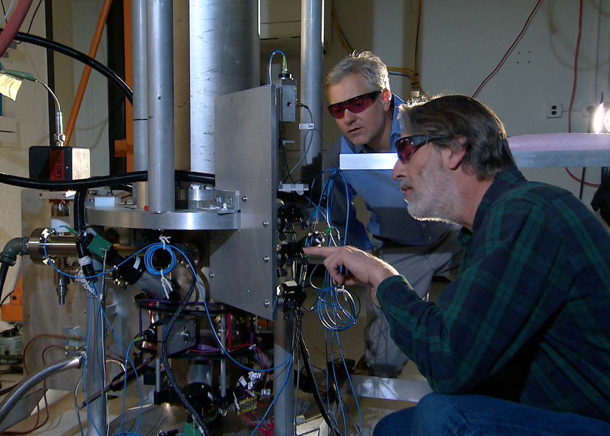 Two scientists standing beside the tall NIST-F2 cesium fountain atomic clock in a laboratory.