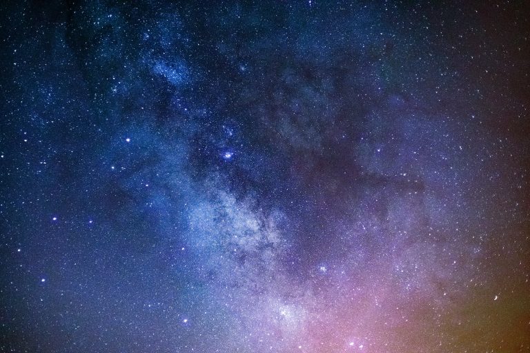 Night sky showing the Milky Way as a dense river of stars, colored blue, purple, and pink.