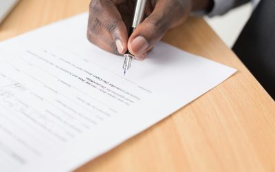 Close-up of a hand signing an official form with a fountain pen, the kind of paperwork a notary or commissioner of oaths would witness.