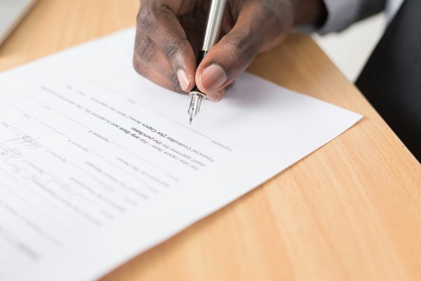Close-up of a hand signing an official form with a fountain pen, the kind of paperwork a notary or commissioner of oaths would witness.