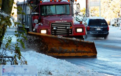 A red plow truck clears a wet winter street, pushing snow toward the curb.