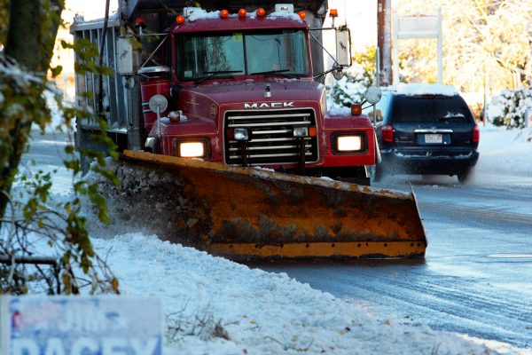 A red plow truck clears a wet winter street, pushing snow toward the curb.