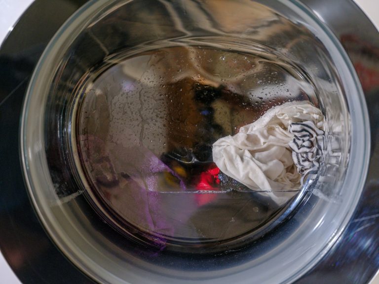 Close-up through the circular glass door of a front-load washer, where dirty water remains in the drum around wet laundry after the machine failed to drain.
