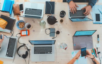 Top view of people sitting down at a table with assorted laptop computers and mobile phones.