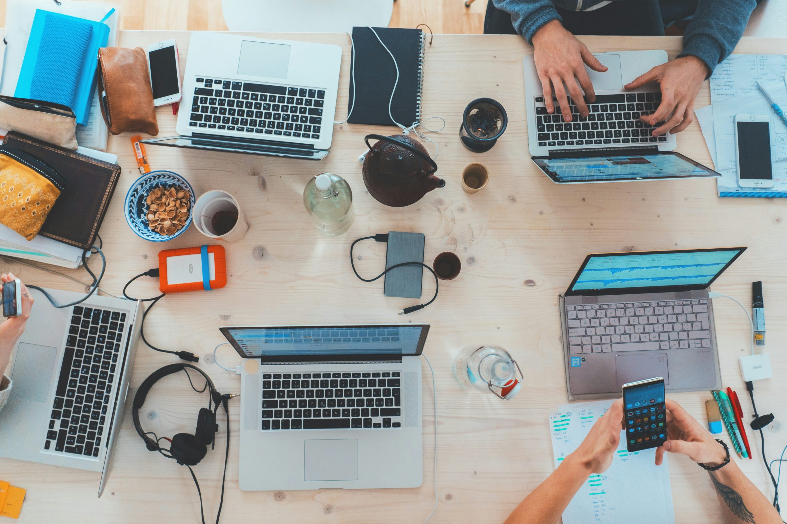 Top view of people sitting down at a table with assorted laptop computers and mobile phones.
