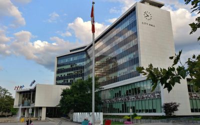 Hamilton City Hall, a white office tower marked “CITY HALL,” with a Canadian flag in front.