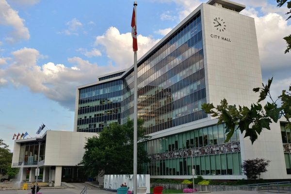Hamilton City Hall, a white office tower marked “CITY HALL,” with a Canadian flag in front.